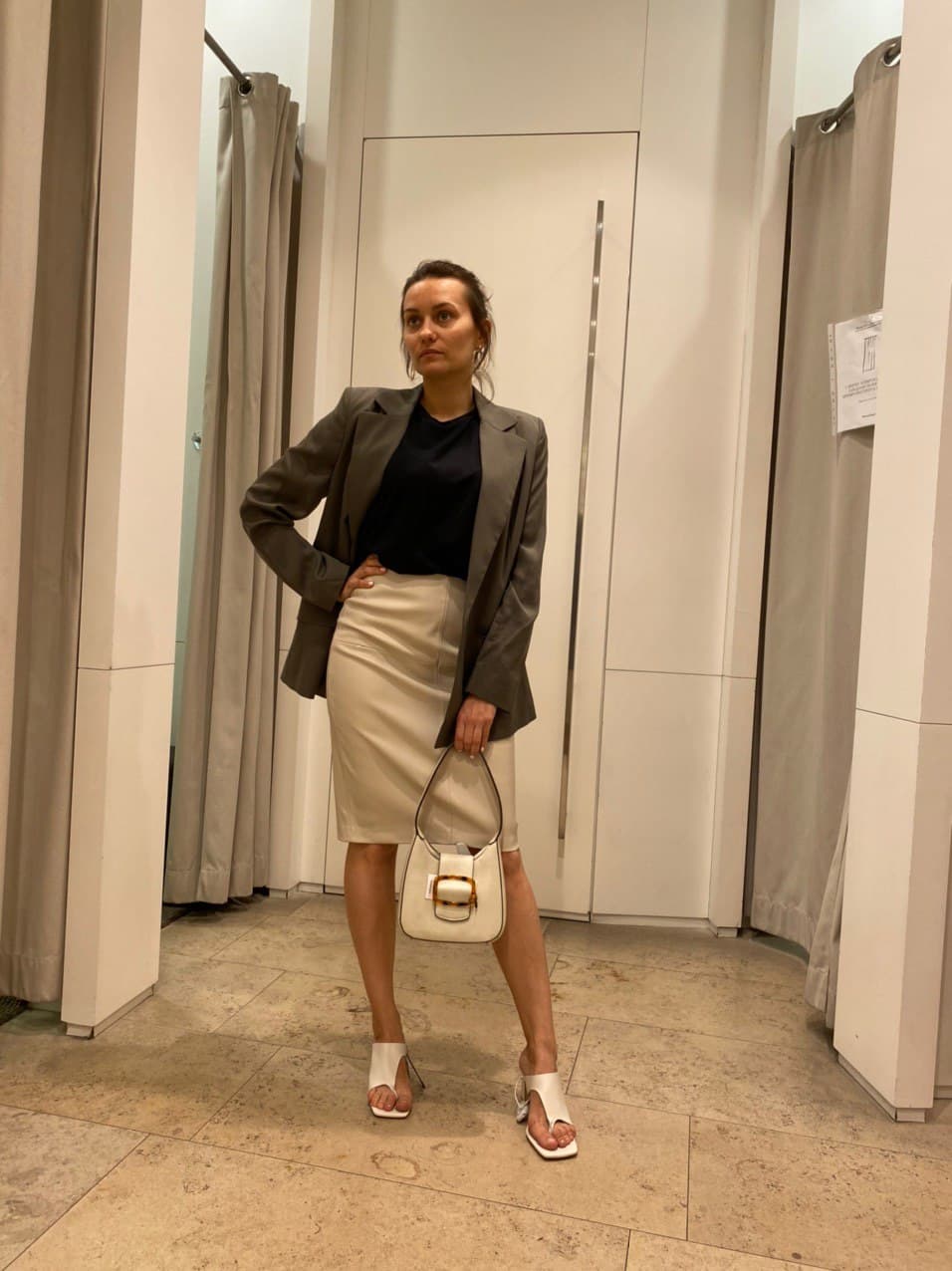 Client trying on a taupe blazer with a cream pencil skirt in a fitting room